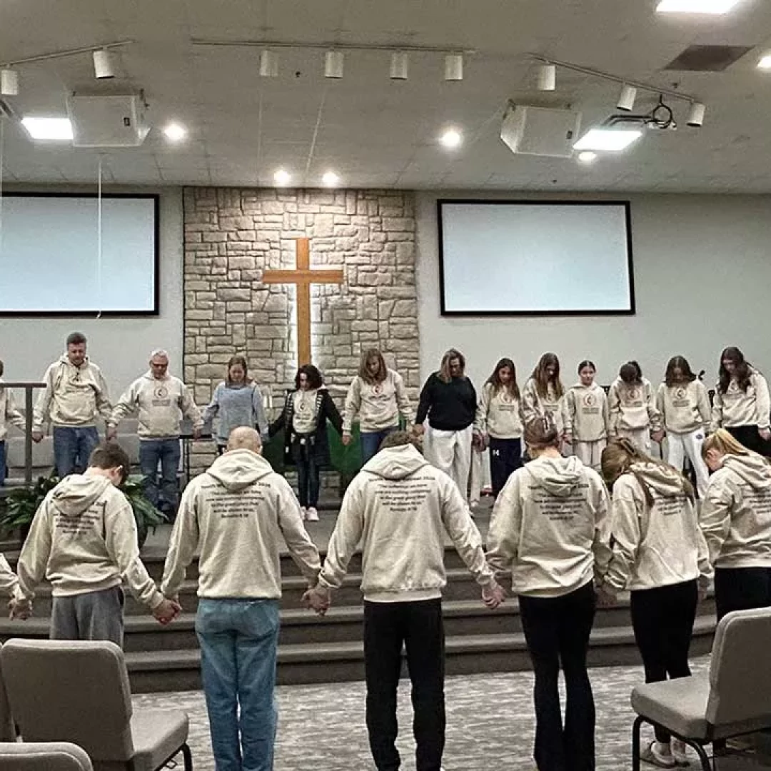 Group holding hands in prayer inside church sanctuary with cross at the front