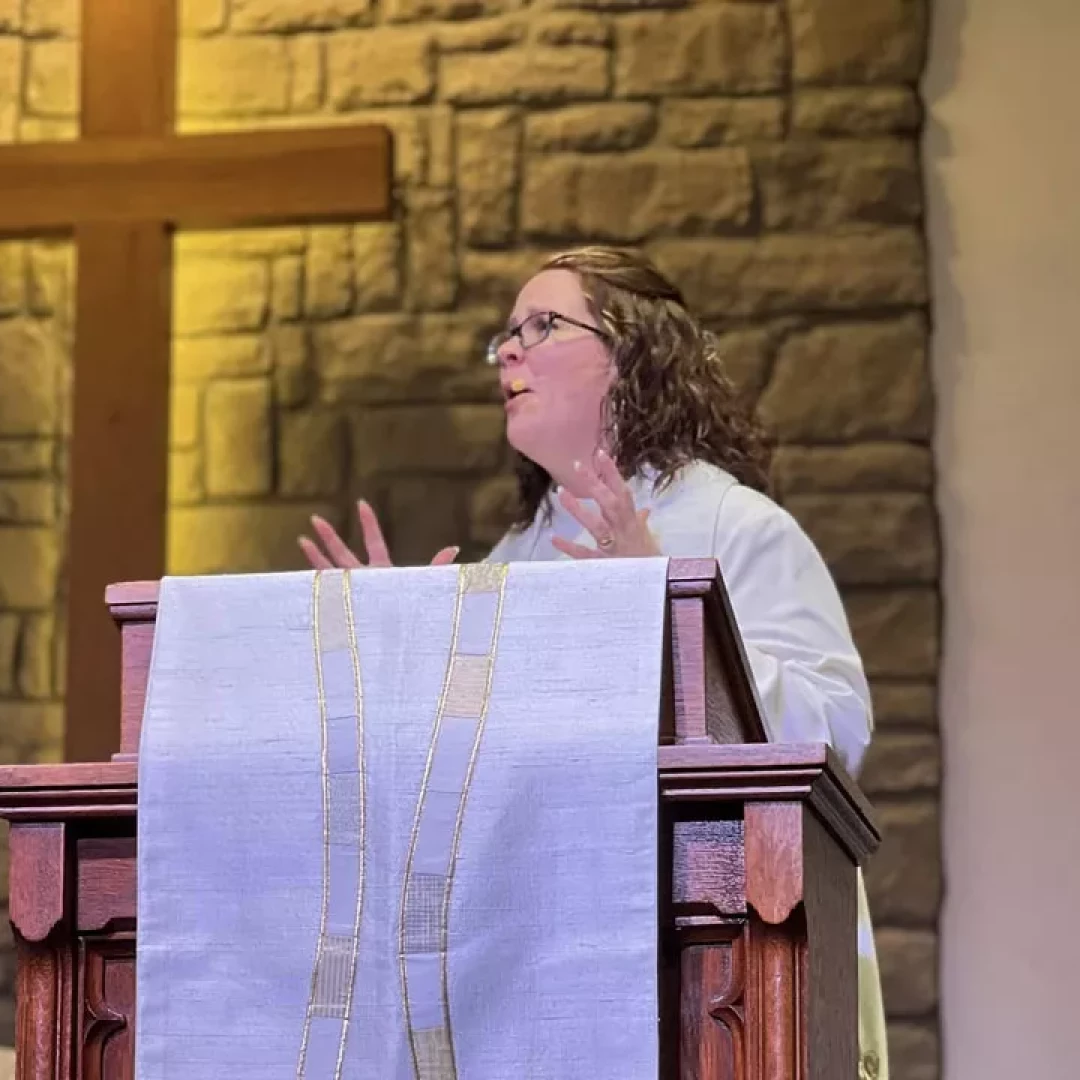 Pastor speaking at pulpit inside church sanctuary with cross in the background
