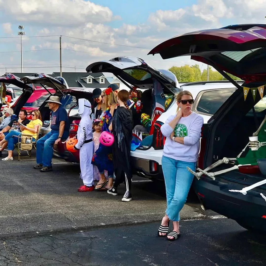 Families and children in costumes at trunk or treat event with decorated cars in parking lot