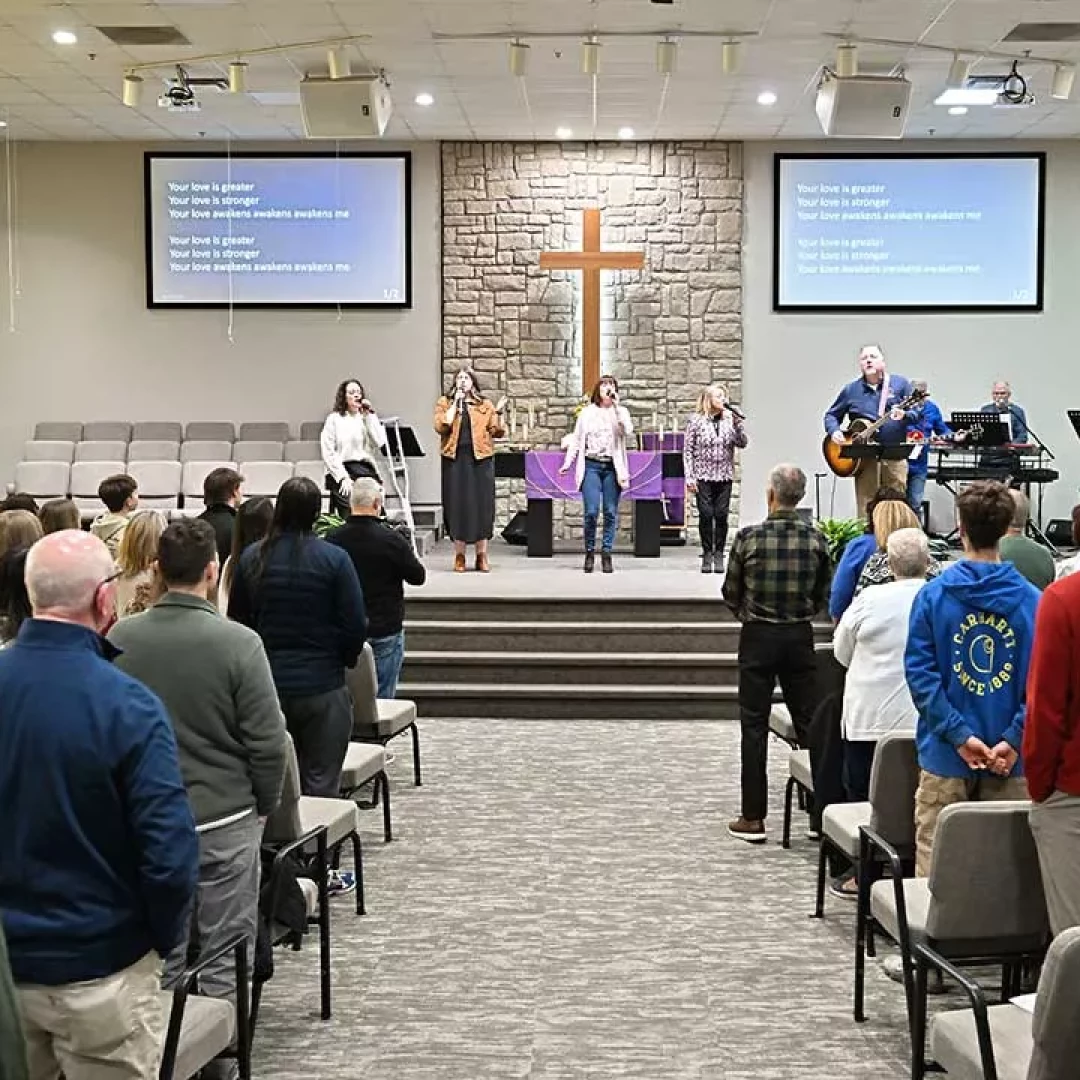 Church congregation standing during worship service with live band and cross at the front