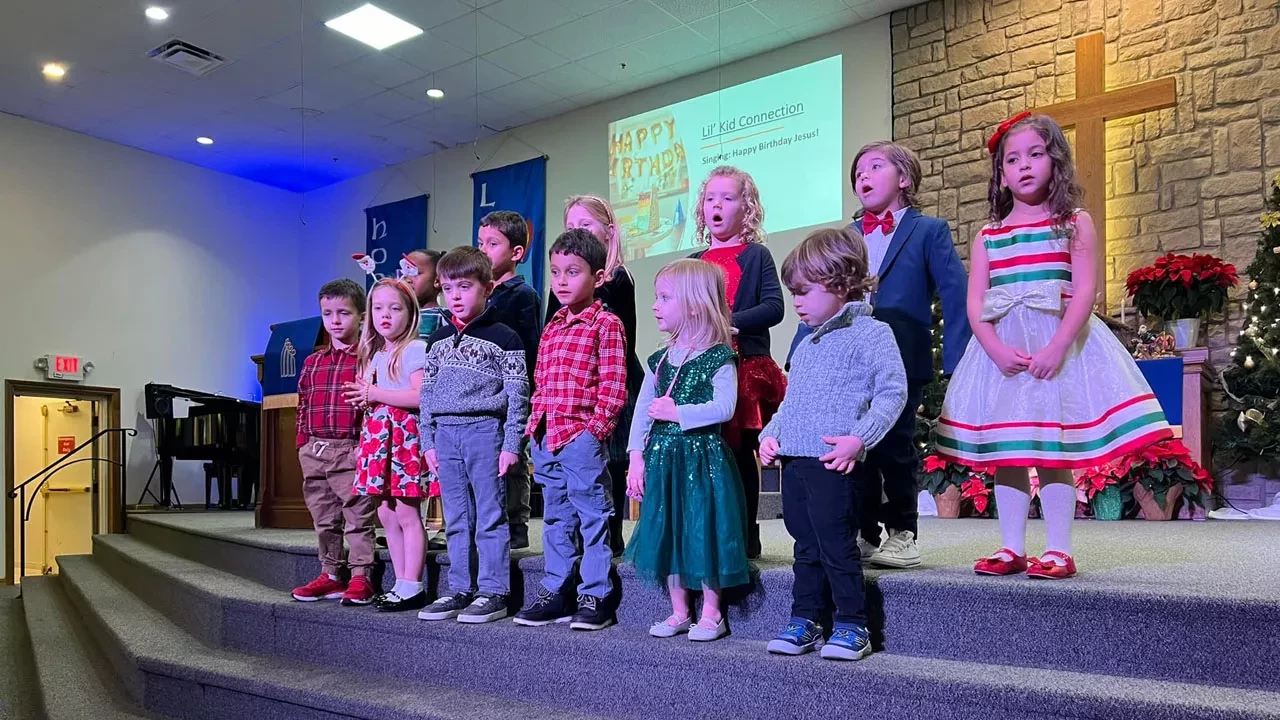 Children performing on stage during church kids program with cross in background