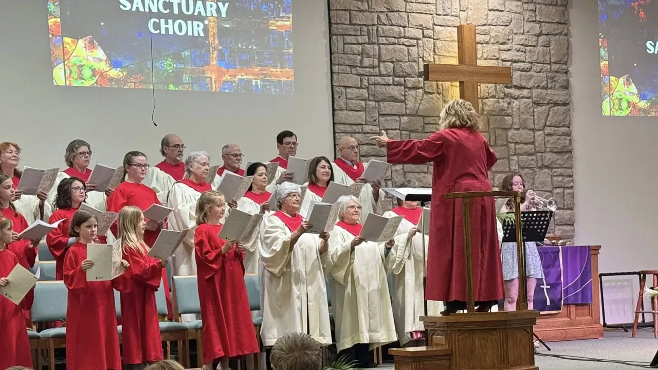Church sanctuary choir singing in robes with director leading in front of cross